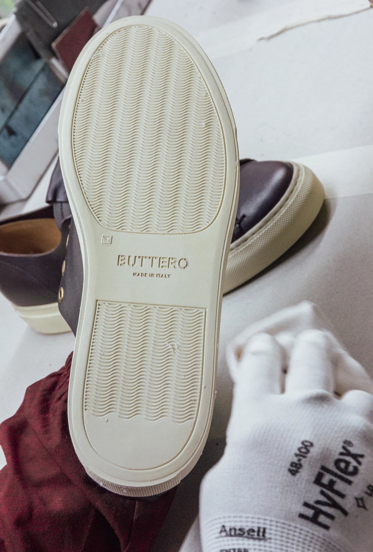 Sole of a Tanino sneaker stamped Buttero, Made in Italy, held by a gloved hand